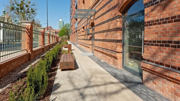 A brick building with a paved walkway, benches, and a metal fence. - Bastion Wałowa 10 | City Center | Parking (Gdańsk)
