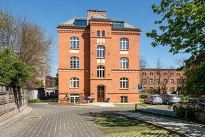 Ein Gebäude aus roten Ziegeln mit einem zentralen Eingang, großen Fenstern und einem gepflasterten Innenhof.