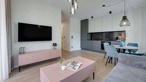 Uma sala de estar moderna com televisão de tela plana, um banco rosa, uma mesa de centro e uma área de jantar com cadeiras e mesa.