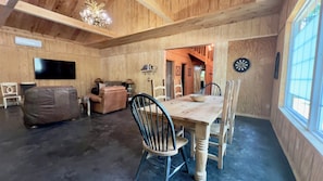 A wooden interior with a dining table, chairs, a sofa, a TV, and a dartboard.