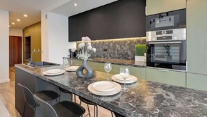 A modern kitchen with a marble countertop, built-in appliances, and a central island with bar seating. - Aura Island 90 Deluxe | River View | Parking (Gdańsk)