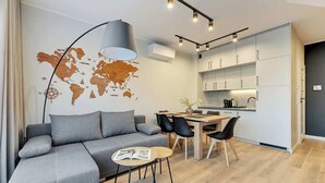 Ein moderner Wohnbereich mit grauem Sofa, einem Esstisch mit Stühlen, einer Weltkarte an der Wand und einer Küchenzeile mit weißen Schränken.