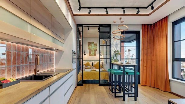 A modern kitchen with a glass backsplash, a wooden countertop, and a dining area with stools. - Doki C80 | Gdańsk Shipyard & Foodhall (Gdańsk)