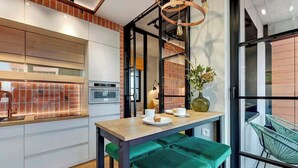 A modern kitchen with a built-in oven, a wooden table with green barstools, and a hanging chair by a large window. - Doki C80 | Gdańsk Shipyard & Foodhall (Gdańsk)