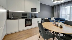 Een moderne keuken met witte kasten, een inbouwoven en een eethoek met een ronde tafel en stoelen.