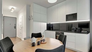 Een moderne keuken met witte kastjes, een zwart aanrecht en een ronde eettafel met stoelen.