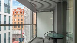 Een balkon met een glazen deur, een ronde tafel en stoelen, met uitzicht op een stadslandschap met gebouwen.