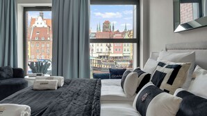 Une chambre d’hôtel avec une grande fenêtre, un lit avec une literie noire et blanche, une petite table avec un vase et un miroir au mur.