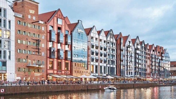 A waterfront hotel with multiple stories, a restaurant on the ground floor, and a canal with a boat. - Deo Plaza 515B | Nice City View | Hotel standard (Gdańsk)