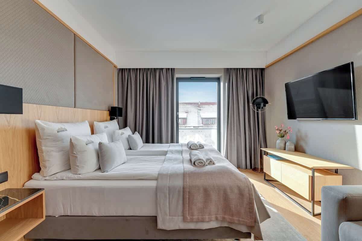 A hotel room with a large bed, a TV, a desk, and a view of the city.