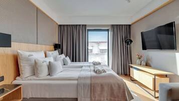 A hotel room with a large bed, a TV, a desk, and a view of the city.