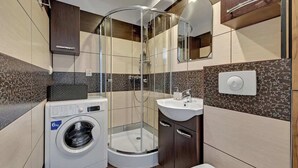 Une petite salle de bain équipée d’un lave-linge, d’une douche à parois de verre et d’un lavabo.