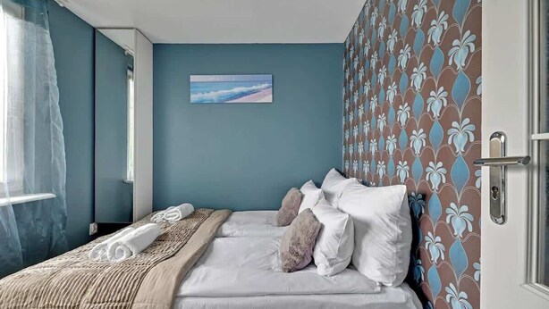 Une chambre à coucher avec un lit, des oreillers, une couverture, un tableau au mur et un papier peint à motifs.