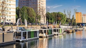 A canal with houseboats docked, surrounded by trees and buildings.