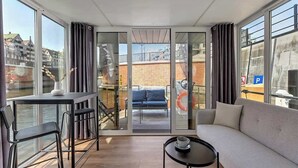 A modern room with a sofa, a small table, and a balcony with a view of buildings and a blue chair.