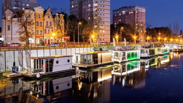 A canal with floating houses, a bridge, and buildings in the background.