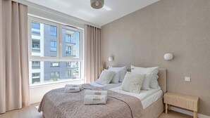 Ein modernes Hotelzimmer mit einem großen Bett, einem Nachttisch, einem Fenster mit Vorhängen und Blick auf die Stadtlandschaft.