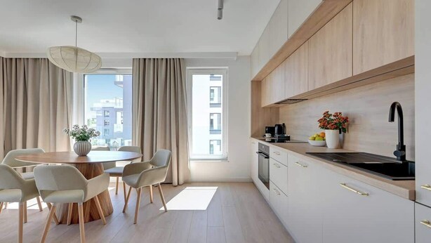 Eine moderne Küche mit Holzschränken, einem schwarzen Spülbecken und einem Essbereich mit rundem Tisch und Stühlen.