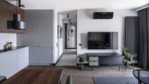 Une cuisine moderne avec des meubles blancs, un coin repas doté d’une table en bois et un espace de vie avec un téléviseur et des plantes.