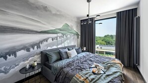 Une chambre à coucher avec un grand lit, une table de chevet, une fresque murale et une fenêtre avec des rideaux.