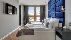 Une chambre d’hôtel moderne avec un grand lit, un téléviseur à écran plat fixé au mur et une vue sur la ville par la fenêtre.