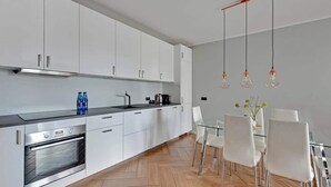 Une cuisine moderne avec des meubles blancs, un four en acier inoxydable, une machine à café et une table à manger en verre, assortie de chaises blanches.