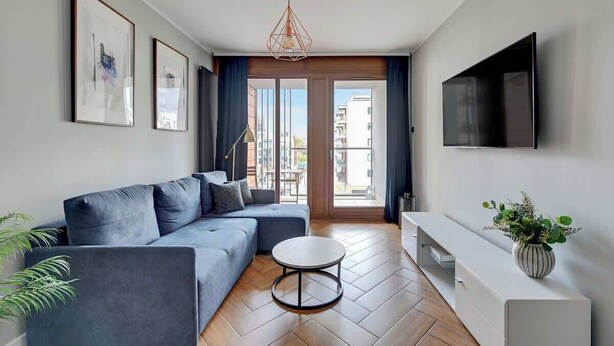 Un salon moderne avec un canapé, une table basse ronde, un téléviseur fixé au mur et une plante posée sur une table d’appoint.
