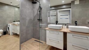 Une salle de bain moderne avec une douche à parois de verre, un grand miroir et un meuble-lavabo en bois doté de deux vasques.
