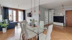 Un salon moderne avec une table à manger en verre, des chaises blanches, un canapé et un téléviseur.