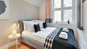 A bedroom with a bed, bedside table, lamp, window with curtains, and a view of the outside. - Ogarna's Bells | Main Old Town | Perfect Stay (Gdańsk)