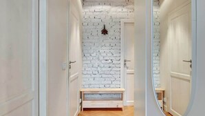 A hallway with white brick walls, a wooden bench, and a mirror on the right wall. - Ogarna's Bells | Main Old Town | Perfect Stay (Gdańsk)