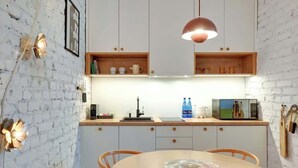 A kitchen with white cabinets, a wooden countertop, a round table, and a hanging pendant light. - Ogarna's Bells | Main Old Town | Perfect Stay (Gdańsk)