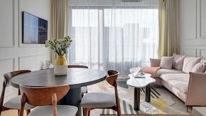 Ein modernes Wohnzimmer mit einem runden Esstisch, Holzstühlen, einer Couch und einem großen Fenster mit Vorhängen.