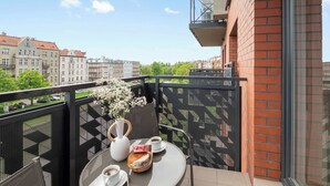 En balkon med et bord dækket til to, en vase med blomster og udsigt over bybilledet.