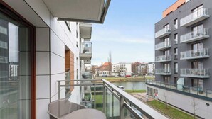 Un appartement moderne doté d’un balcon, offrant une vue sur une rivière et sur le paysage urbain en arrière-plan.