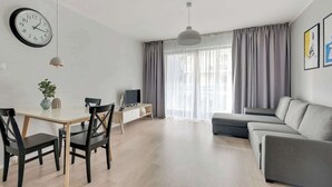 Un salon moderne comprenant un coin repas, un canapé gris, un téléviseur et une horloge murale.