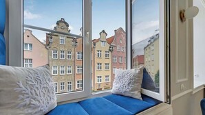Ein Zimmer mit Fensterbank, weißen Kissen und Blick auf bunte Gebäude.