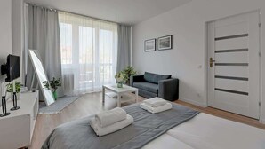 Een moderne hotelkamer met een bed, een bank, een televisie, een bureau en een groot raam met gordijnen.