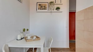Een eetgedeelte met een witte tafel, stoelen, een dienblad met kopjes, een vaas met bloemen en een klok aan de muur.