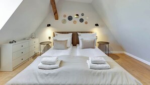 A bedroom with a sloped ceiling, a bed with white linens, two bedside tables, a dresser, and a wall-mounted light fixture. - Grunwaldzka Attic | Great Location | Family Stay (Gdańsk)