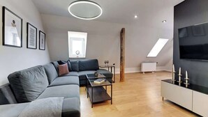 A modern living room with a sectional sofa, a coffee table, a TV, and a wooden accent wall. - Grunwaldzka Attic | Great Location | Family Stay (Gdańsk)