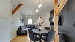 A modern living room with a round dining table, dark sofas, and a TV mounted on the wall. - Grunwaldzka Attic | Great Location | Family Stay (Gdańsk)