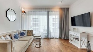 Una sala de estar moderna con un sofá, una mesa redonda, un televisor y un amplio ventanal con cortinas.