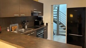 A modern kitchen with dark cabinets, a stainless steel sink, a black refrigerator, and a staircase leading to an upper level. - Roof terrace apartment in Avignon (Avignon)
