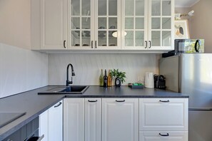 Eine Küche mit weißen Schränken, einer schwarzen Arbeitsplatte, einem Edelstahlkühlschrank und einer Mikrowelle.