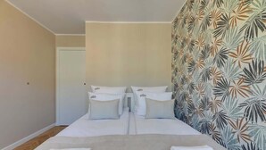 Ein Hotelzimmer mit einem Bett, zwei Kissen, einem Nachttisch und einer Wand mit einem Blattmuster.