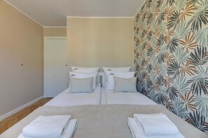 Ein Hotelzimmer mit einem Bett, zwei Kissen, einem Nachttisch und einer Wand mit einem Blattmuster.
