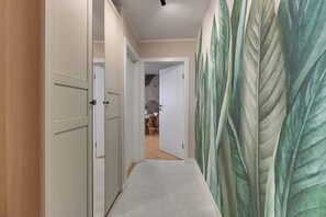 Ein Korridor mit einer Holztür, einer weißen Tür und einer Wand mit einem Blattmuster.