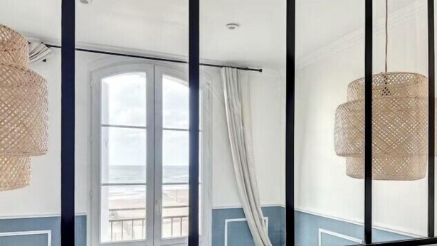 Una habitación con un ventanal grande, un balcón y dos lámparas de mimbre.