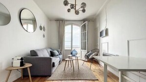 Una sala de estar moderna con sofá, mesa de comedor, televisor y un ventanal grande.
